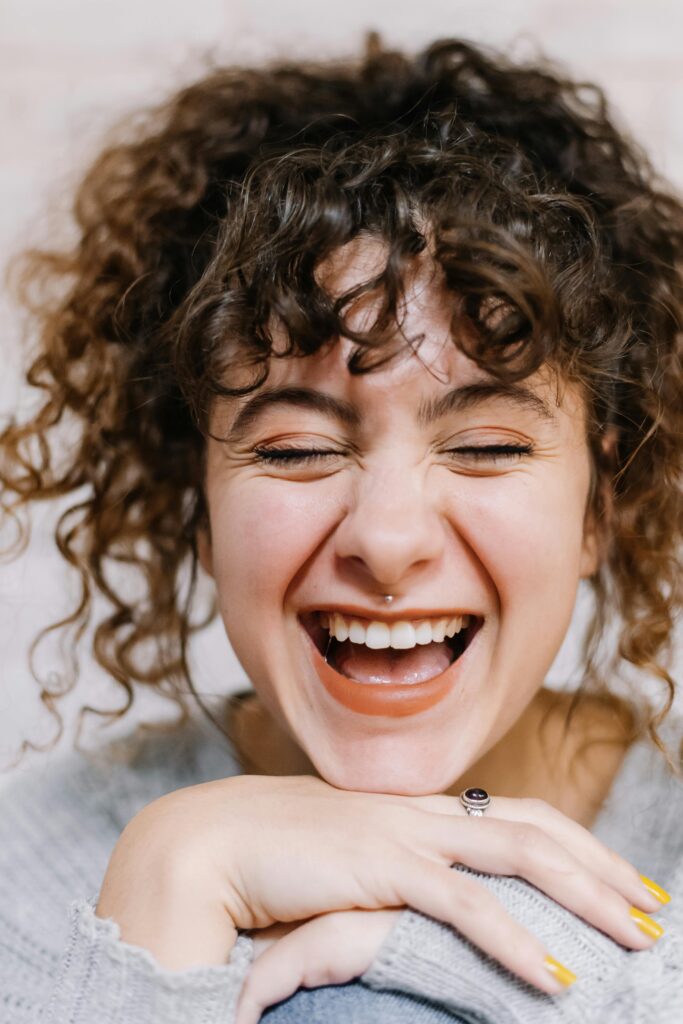 Close-up portrait of a smiling woman with curly hair and vibrant expression.
